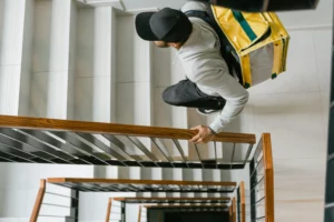 Livreur montant un escalier avec un sac à dos lourd, illustrant les bienfaits de l'entraînement fonctionnel sur les mouvements de la vie quotidienne - Fitspro Equipement