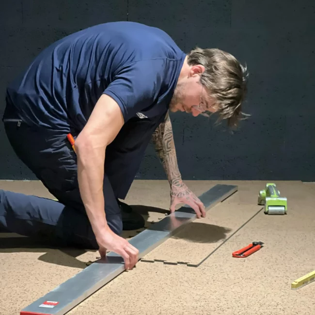 Technicien Fitspro Équipement ajustant avec précision les découpes d'un revêtement de sol technique pour salle de sport.