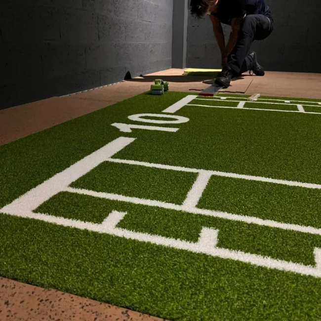Gros plan sur une piste en gazon synthétique vert avec marquages pour l'entraînement fonctionnel. Fitspro Equipement