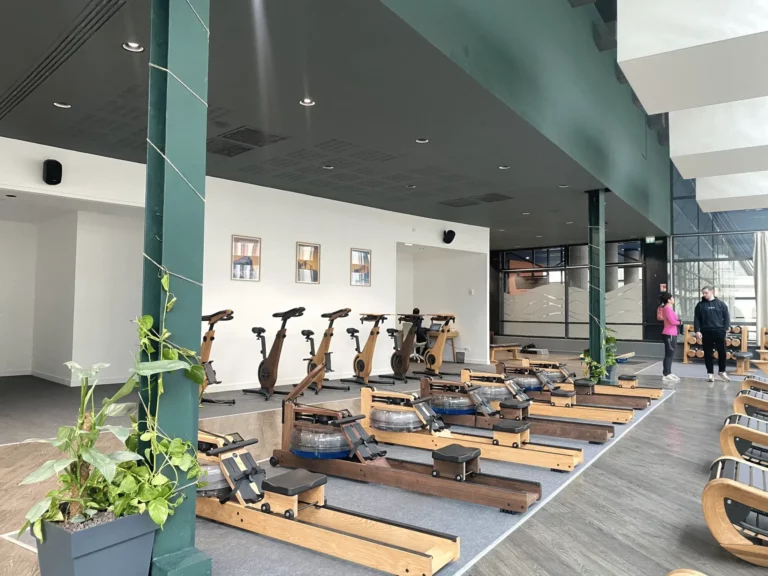 Zone de cardio-training équipée de rameurs à eau et vélos d'appartement en bois dans un espace lumineux - Fitspro Equipement
