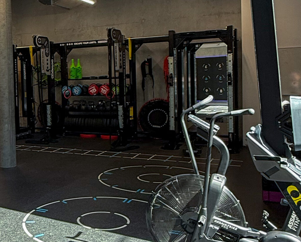 Zone de cross-training équipée d'un Assault AirBike, d'une cage de musculation avec kettlebells et d'un marquage au sol pour l'entraînement fonctionnel - Fitspro Equipement