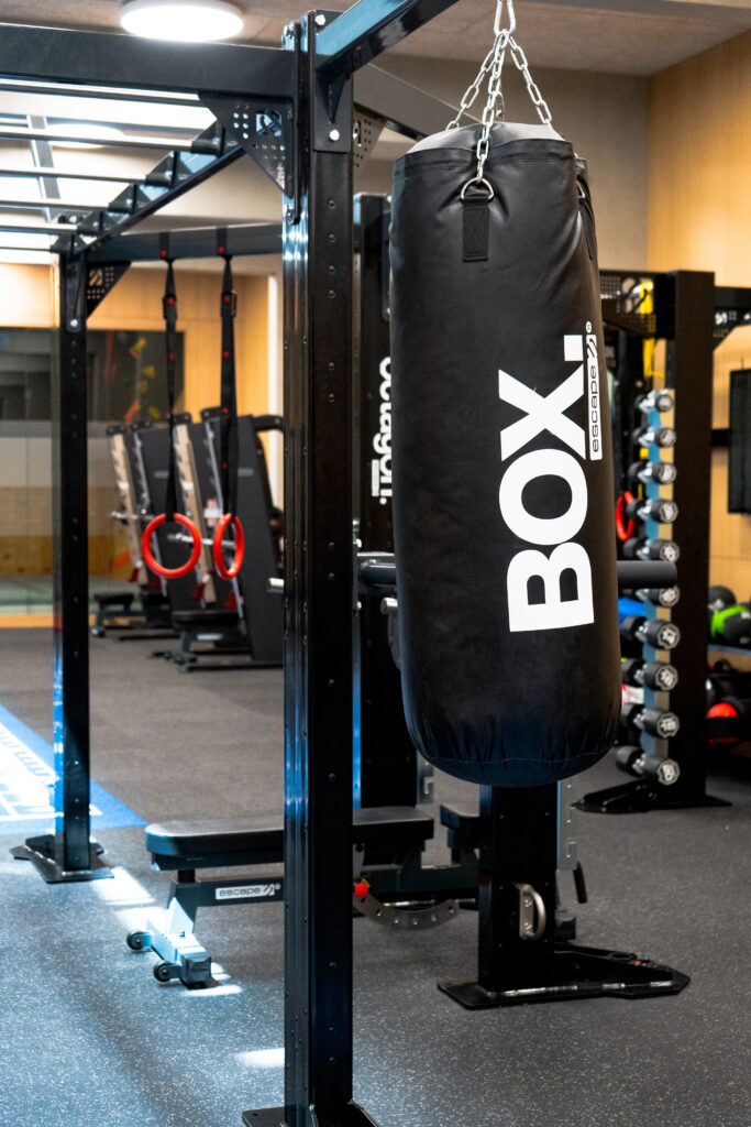 Sac de frappe noir suspendu dans la zone de combat et de cross-training d'une salle de sport moderne - Fitspro Equipement